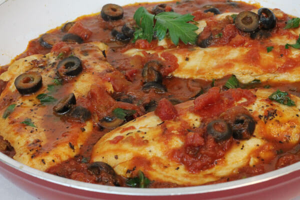 chicken cooked in a skillet with tomatoes, garlic and black olives